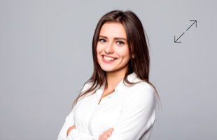 Frau mit langen braunen Haaren in weißem Hemd lächelt vor grauem Hintergrund.