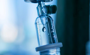 Nahaufnahme eines Tropfens in einer Infusionsflasche mit blauer Beleuchtung.