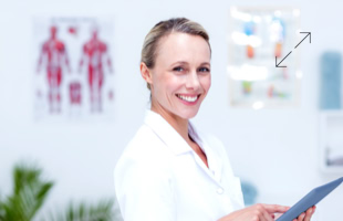 Frau in weißem Kittel lächelt und hält ein Tablet, im Hintergrund sind anatomische Poster und Pflanzen zu sehen.