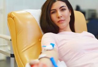 Frau sitzt auf einem gelben Stuhl und spendet Blut, mit einem Verband am Arm.