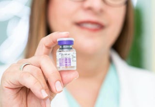 Eine Person hält ein kleines Fläschchen mit lila Deckel in der Hand.