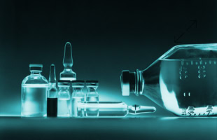 Mehrere Glasfläschchen und Ampullen, teilweise gefüllt, auf einer Oberfläche; eine große Flasche liegt seitlich.