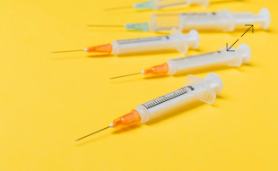 Mehrere Spritzen mit Nadeln auf gelbem Hintergrund.