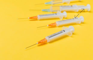 Sechs Spritzen mit Nadeln auf gelbem Hintergrund.