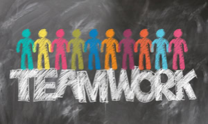 Bunte Figuren stehen auf einer Tafel über dem Wort "TEAMWORK".