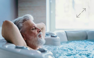 Älterer Mann mit grauem Haar und Bart entspannt sich in einem Whirlpool, mit geschlossenen Augen und Händen hinter dem Kopf.