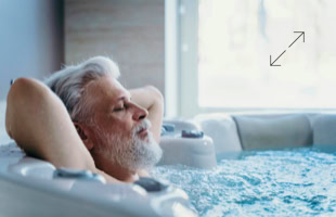 Älterer Mann mit grauem Haar und Bart entspannt sich in einem Whirlpool, mit geschlossenen Augen und den Armen hinter dem Kopf verschränkt.