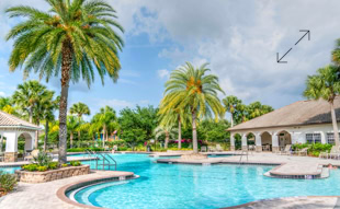 Ein Außenpool mit Palmen, umgeben von Gebäuden mit weißen Wänden und grauen Dächern unter einem bewölkten Himmel.