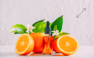 Orangen und eine Flasche mit Pipette, umgeben von grünen Blättern und weißen Blüten, auf hellem Hintergrund.