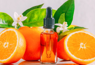 Eine Flasche mit Pipette steht zwischen zwei Orangenhälften und einer ganzen Orange, umgeben von grünen Blättern.
