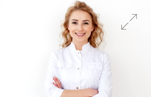 Frau mit lockigem Haar in weißem Hemd, lächelnd mit verschränkten Armen vor weißem Hintergrund.