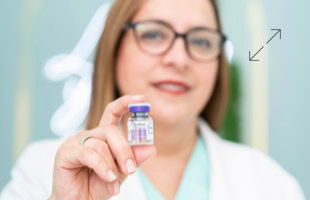 Frau mit Brille hält ein kleines Fläschchen in der Hand, unscharfer Hintergrund.