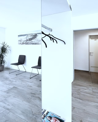 helles, sonniges ambiente im wartezimmer mit garderobe, stuehlen und blick in den flur