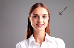 Eine lächelnde Person mit langen braunen Haaren in einem weißen Hemd vor einem grauen Hintergrund.