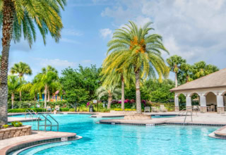Ein Außenpool mit Palmen, umgeben von Gebäuden mit Bögen und einem bewölkten Himmel im Hintergrund.