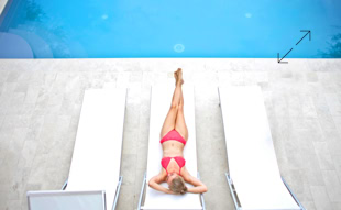 Person in rotem Badeanzug liegt auf einer Sonnenliege neben einem Pool.