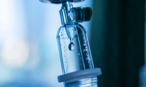 Nahaufnahme eines Tropfens in einem Infusionsschlauch mit blauer Beleuchtung.